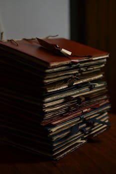 A stack of vintage folders tied with ribbons sits on a wooden desk, exuding a sense of nostalgia.